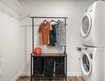 a laundry room with a washer and dryer and a shelf with clothes hanging